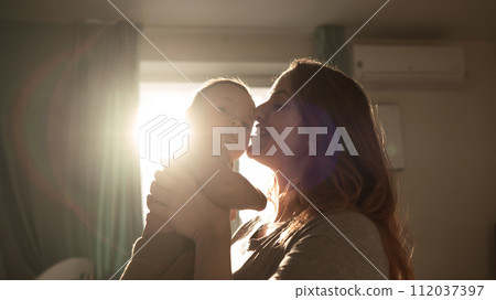 A Caucasian woman tenderly kisses her newborn son in the morning rays of sunlight. 112037397