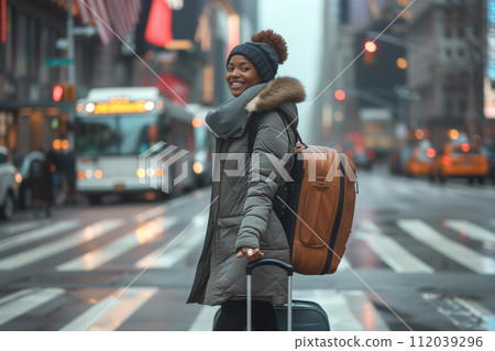 Cheerful African American woman with wheeled luggage crosses the road Cheerful African American woman with wheeled luggage crosses the road 112039296