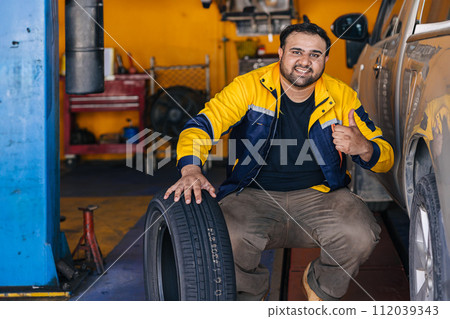Portrait Indian man worker in garage auto mechanic happy work car service replace tyre vehicle maintenance Portrait Indian man worker in garage auto mechanic happy work car service replace tyre vehicle maintenance 112039343