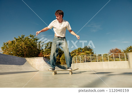 Excited young man riding skateboard in skate park on sunny day. Extreme sport concept 112040159