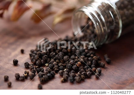 Black peppercorns spilling out of a transparent container Black peppercorns spilling out of a transparent container 112040277