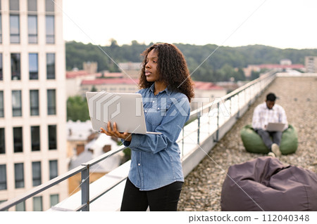 Business woman standing on roof top outdoors and typing on modern laptop. Business woman standing on roof top outdoors and typing on modern laptop. 112040348