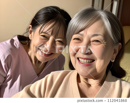 An old woman takes a commemorative photo with a friend on her smartphone in a Japanese-style room at an inn. An old woman takes a commemorative photo with a friend on her smartphone in a Japanese-style room at an inn. 112041868