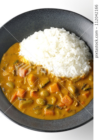 An overhead shot of curry rice with lots of vegetables such as pork, pumpkin, and carrots against a white background 112042166