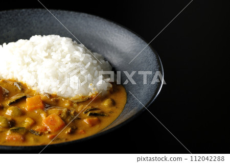 一張咖哩飯的照片，上面有大量蔬菜，如豬肉、南瓜和胡蘿蔔，背景為黑色 112042288