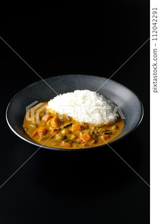 A photo of curry rice with lots of vegetables such as pork, pumpkin, and carrots against a black background 112042291