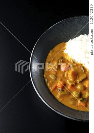 An overhead shot of curry rice with lots of vegetables such as pork, pumpkin, and carrots against a black background An overhead shot of curry rice with lots of vegetables such as pork, pumpkin, and carrots against a black background 112042359