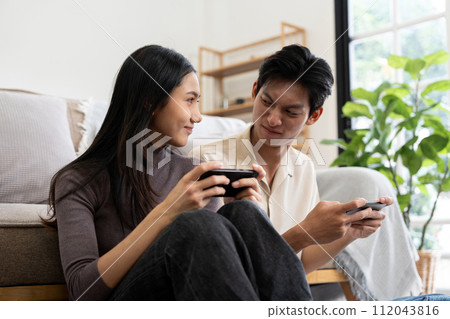 Happy couple asian young women happy enjoy playing match game online game happy relax smile laugh joy fun video gaming app. on couch in living room at home Happy couple asian young women happy enjoy playing match game online game happy relax smile laugh joy fun video gaming app. on couch in living room at home 112043816