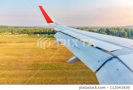 View of airplane wing, blue skies and green land during landing. Airplane window view. 112043930