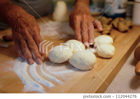 Preparation of homemade fruit dumplings with plums. Czech specialty of sweet good food. Dough on kitchen wooden table with hands. 112044276