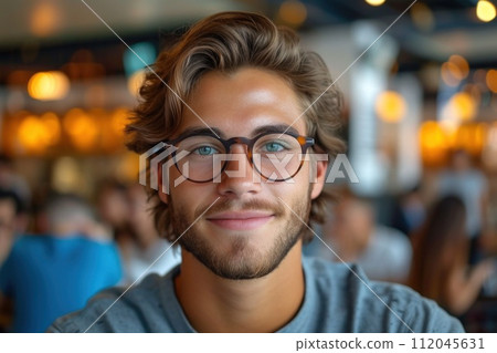 A happy young man with glasses and facial hair smiling at the camera 112045631