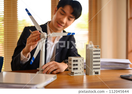 Young businessman looking at wind turbine model, working on new alternative energy project at office space Young businessman looking at wind turbine model, working on new alternative energy project at office space 112045644