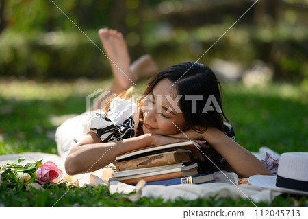 Beautiful young woman falling asleep on a stack of books, enjoys nature and warm weather 112045713