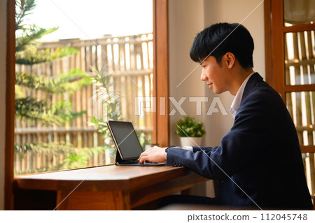 Handsome young businessman drinking hot coffee and reading email on digital tablet at cafe 112045748