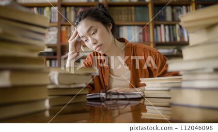 Upset asian female student sitting behind stacks of books, academic pressure 112046098