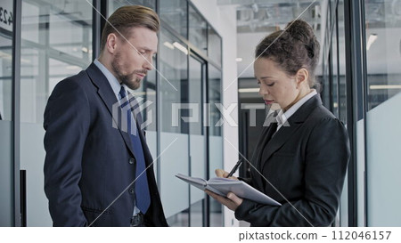 Two company employees discussing business tasks, woman taking notes, teamwork Two company employees discussing business tasks, woman taking notes, teamwork 112046157