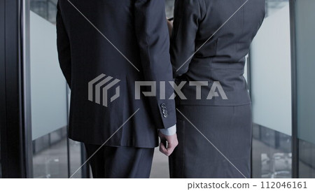 Back view male and female colleagues standing side by side in hall of office building, teamwork Back view male and female colleagues standing side by side in hall of office building, teamwork 112046161