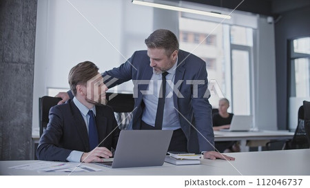 Friendly manager communicating with male colleague, corporate office atmosphere Friendly manager communicating with male colleague, corporate office atmosphere 112046737