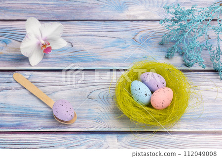 Nest with colored Easter eggs and an orchid flower on the wooden background. Nest with colored Easter eggs and an orchid flower on the wooden background. 112049008