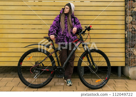 European stylish woman in an informal look with dreadlocks and piercings moves around the city on a 112049722