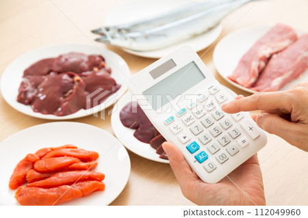 Middle-aged woman holding food containing a lot of B vitamins and a calculator 112049960