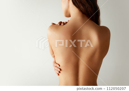 Close up. Rear view of half-naked woman in beige underwear standing hug herself against grey studio background. Body positivity. Close up. Rear view of half-naked woman in beige underwear standing hug herself against grey studio background. Body positivity. 112050207