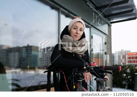 A young woman dressed in winter walks around the city with a bicycle 112050510