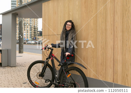 A pretty young woman with a dreadlocked hairstyle rides a bicycle and stops to rest 112050511