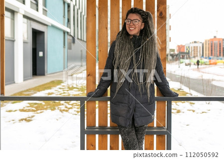 A pretty young woman with a dreadlocked hairstyle dressed in a winter jacket walks around the city A pretty young woman with a dreadlocked hairstyle dressed in a winter jacket walks around the city 112050592