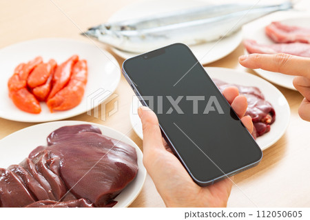 A middle-aged woman eats foods rich in B vitamins and uses a smartphone. 112050605