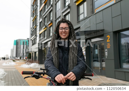 Lifestyle concept, young European woman with informal dreadlocks hairstyle riding a bicycle 112050634