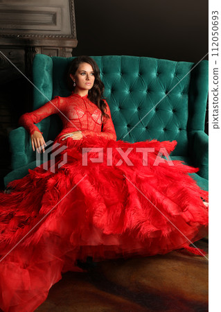 Fashion portrait of beautiful stylish woman wearing red evening gown sitting  112050693