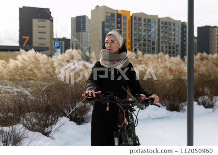 Young woman dressed warmly with scarf and headband rides a bicycle in winter Young woman dressed warmly with scarf and headband rides a bicycle in winter 112050960