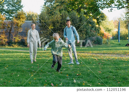 a family mom and 2 sons are having fun, running in the park and jumping. Sons, children, mom, run, play, rejoice, enjoy nature in summer. Family teamwork. Happy family team, running together in field 112051196