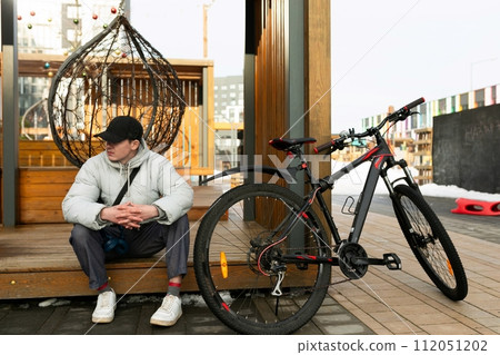 A man in a cap and a warm jacket stands with a rental bicycle 112051202
