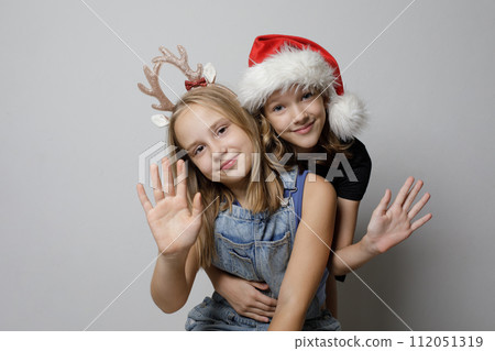 Christmas portrait of happy kid girls best friends hugging on gray background Christmas portrait of happy kid girls best friends hugging on gray background 112051319