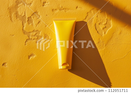 A bright yellow lotion tube casts a shadow on a textured yellow table, skincare in the sunny summer 112051711