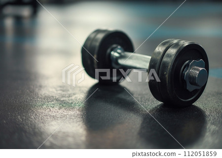 Metal dumbbell with a textured grip on the floor in the gym, fitness and strength training 112051859