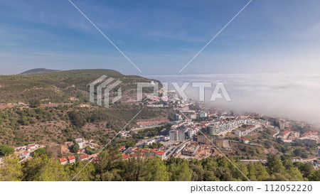 Panorama showing aerial View of Sesimbra Town and Port covered by fog timelapse, Portugal. 112052220