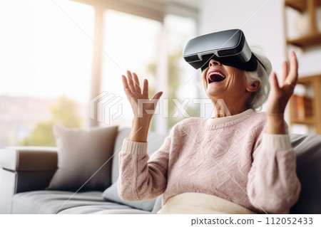 senior woman using virtual reality glasses and sitting on the couch at home 112052433