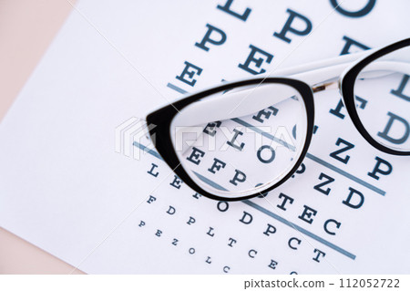 Vision glasses with black frames on a Snellen chart close up Vision glasses with black frames on a Snellen chart close up 112052722