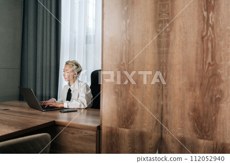 Remote view of focused middle-aged businesswoman sitting at desk typing working on laptop, browse wireless internet. Concentrated elegant senior female employee consult client online using computer. 112052940