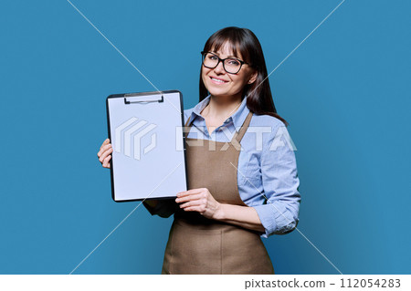 Smiling woman worker, owner in apron showing blank sheet of paper on clipboard Smiling woman worker, owner in apron showing blank sheet of paper on clipboard 112054283