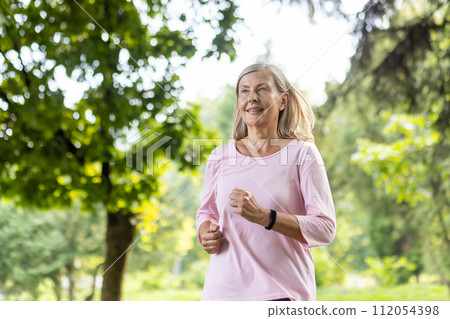 Active senior woman with a smile jogging in a lush green park, embracing fitness and health in the golden years. Active senior woman with a smile jogging in a lush green park, embracing fitness and health in the golden years. 112054398