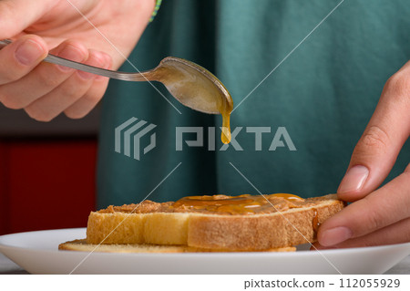 a drop of honey dripping from a spoon onto a peanut butter sandwich, close up 112055929
