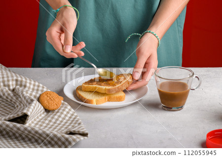 Woman's hands puting honey with spoon on a toast with peanut butter to make a sandwich for breakfast Woman's hands puting honey with spoon on a toast with peanut butter to make a sandwich for breakfast 112055945