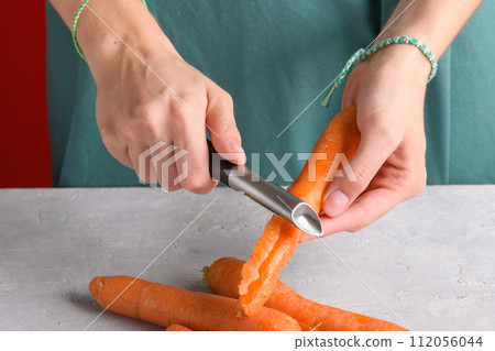 woman hands peeling fresh raw carots on gray ktchen table, close up, preparing food lifestyle 112056044