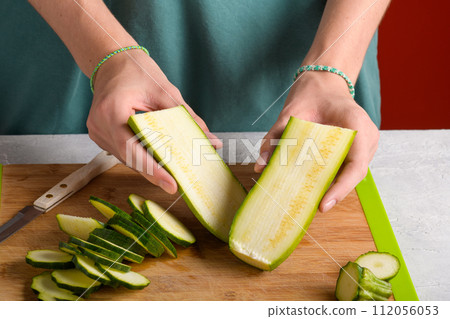 Woman's hands cutting zucchini on wooden cutting board at home, preparing healthy food, close up 112056053