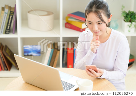 一位女士一邊看電腦一邊使用智慧型手機 112056270