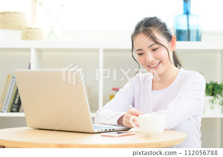A woman looking at a computer while taking notes 112056788